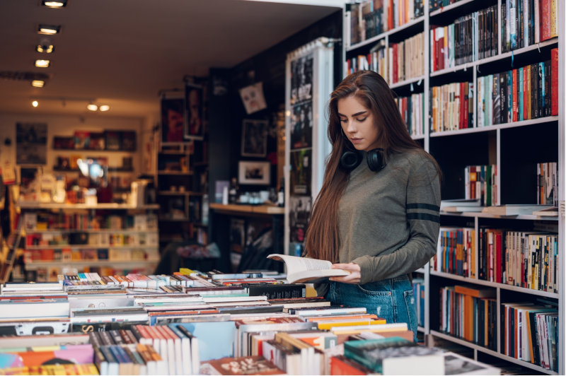 Ragazza sfoglia un libro tra gli scaffali di una libreria