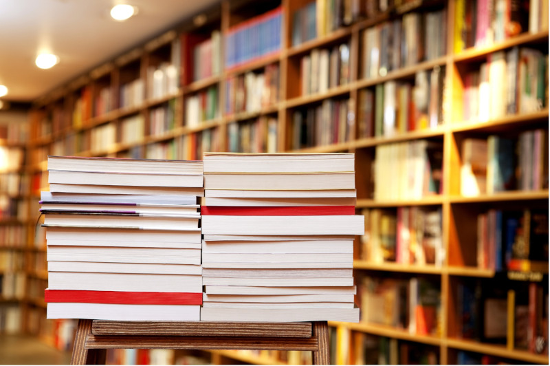 Pile di libri esposti su uno sgabello davanti agli scaffali di una libreria.